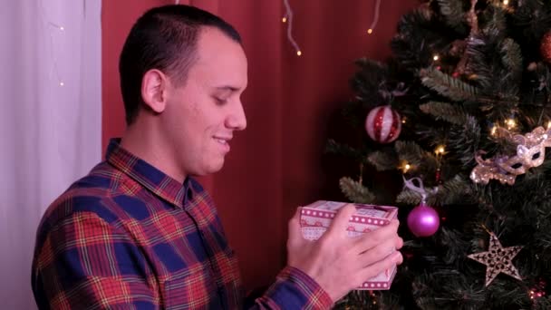 Muž s vánočním kloboukem si přeje a otevře vánoční dárkový balíček. koncepce dovolených a nového roku. dívka je šťastná a usmívá se s vánočním dárkem v ruce. koncept dovolené a nový rok. — Stock video
