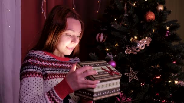 Meisje met KERSTMUTS maakt van wensen en opent een kerst cadeau pakket. concept van de feestdagen en Nieuwjaar. het meisje is gelukkig en glimlacht met de gift van Kerstmis in de hand. — Stockvideo
