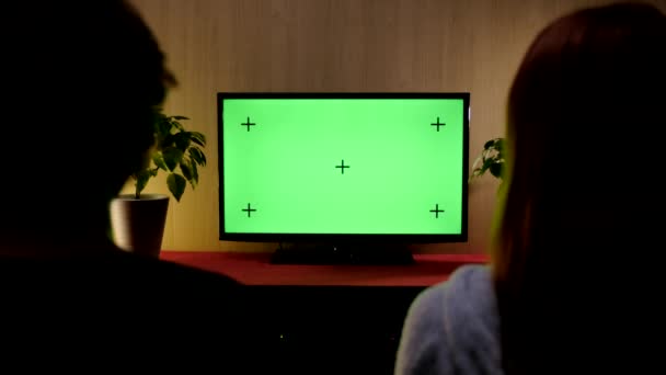 Pareja mira la pantalla de televisión maqueta verde mientras está sentado en un sofá en la sala de estar. — Vídeo de stock