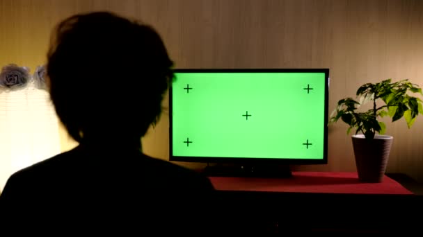 Zicht vanuit de achterste vrouw zittend in de woonkamer en tv kijkend met groen scherm. Chroma sleutel. Binnenshuis — Stockvideo