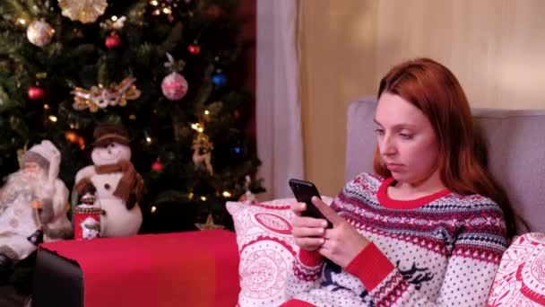 Portrait d'une femme triste et solitaire assise près du sapin de Noël avec téléphone portable. concept de vacances et nouvelle année . — Video