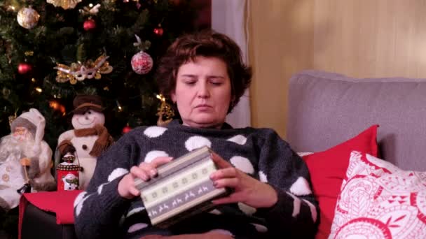 Julklapp - Sorglig kvinna liggande på en soffa nära julgranen, öppning gåva besviken och olycklig. begreppet semester och nytt år. — Stockvideo