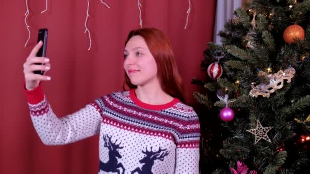 Junge Frau macht Selfie-Foto in der Nähe des geschmückten Weihnachtsbaums. Konzept von Feiertagen, Weihnachten und Neujahr. — Stockvideo