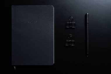 Siyah biçim seti: Siyah arkaplan üzerinde not defteri, kalem ve kağıt ataçları