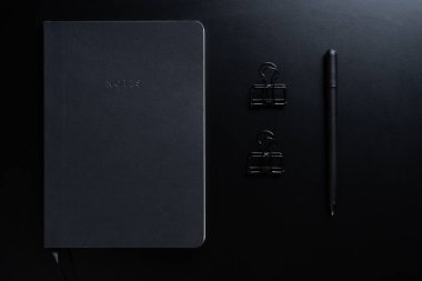 Siyah biçim seti: Siyah arkaplan üzerinde not defteri, kalem ve kağıt ataçları