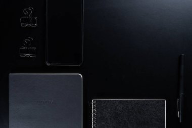 Siyah biçim seti: Siyah arkaplan üzerinde not defteri, kalem ve kağıt ataçları