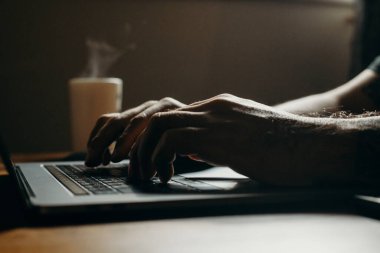 Karanlık bölgede dizüstü bilgisayar kullanan bir adamın yakın çekim görüntüsü. Kahveyle fazla mesai yapıyorum..