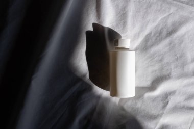 Açık renk kumaş arka planda beyaz bir şişe ve gölge. Kapaklı Kimyasal Çözücü Şişesi