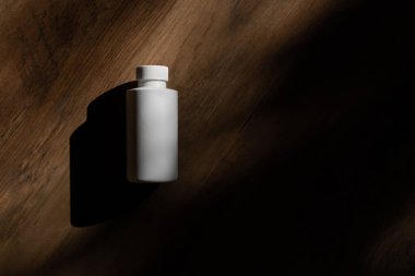 Ahşap arka planda beyaz bir şişe ve gölge. Kapaklı Kimyasal Çözücü Şişesi