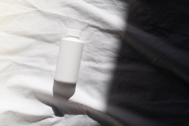 Açık renk kumaş arka planda beyaz bir şişe ve gölge. Kapaklı Kimyasal Çözücü Şişesi