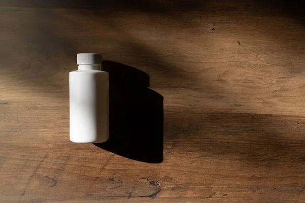 White bottle on a wooden background and shadow. Chemical Solvent Bottle with Cap