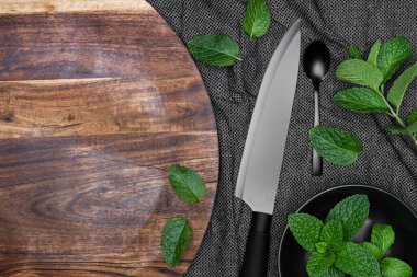 Siyah kase, taze otlu bıçak ve kaşık, arka planda nane şekeri ve tahta doğrama tahtası. Kopyalama alanı.