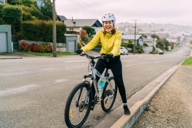 18 / 04 / 2020-Asyalı kadın dağ bisikletiyle yokuş yukarı gidiyor. Bir kadın çok yorgun ve Yeni Zelanda 'nın Oamaru şehrinde sokakta duruyor..