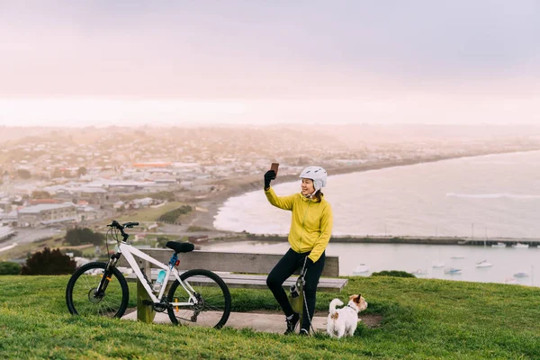 Asian woman making uphill with mountain bike. A woman taking a picture at lookout point with a dog at Oamaru, New Zealand.