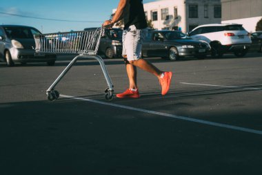 Araba parkında bakkaldan alınmış bir alışveriş arabasını iten adamın yarı vücut portresi..