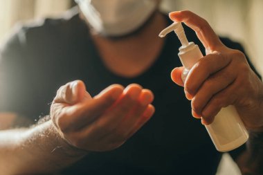 Coronavirus. Coronavirus 'u, Covid-19' u, gribi önlemek için tıbbi koruyucu maske takan adam evde dezenfektan jöle ile ellerini temizliyor. Jel şişesi. Virüs ve hastalık koruması.