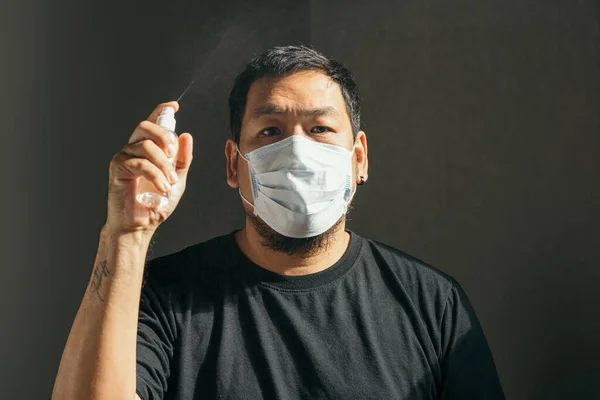 Coronavirus. Man wearing in medical protective mask spraying with sanitizer spray in house to prevent Coronavirus, Covid-19, flu. Spray bottle. Virus and illness protection. Focus at the face.