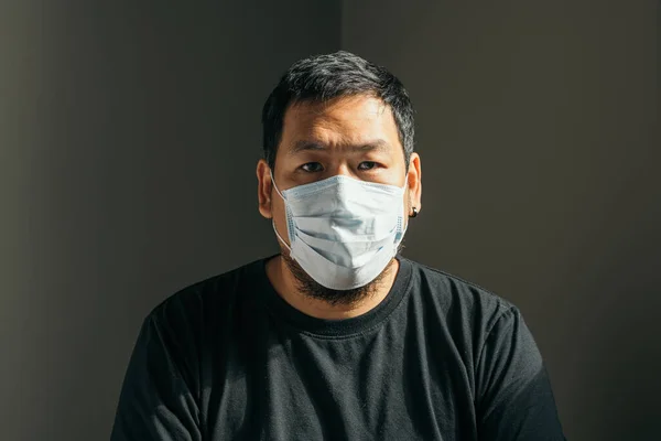 Asyalı adam koruyucu maske takıyor ve evdeki kameraya bakıyor. Corona Virüsü Konsepti.