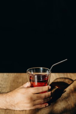 Elinde bir bardak kırmızı tatlı içecekle metal kamışla ya da ahşap masada paslanmaz saman tutan bir adam..