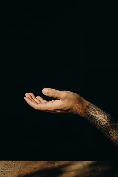 Open hand gesture of male hand on dark background.
