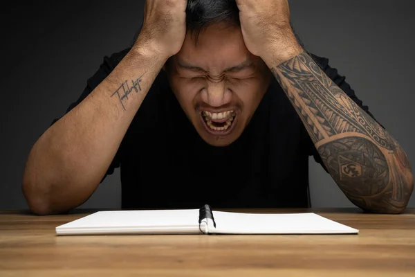 Asian man posing as angry face on wooden table. Concept about wo