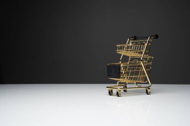 Beyaz masanın üstünde altın renkli küçük boş alışveriş arabası veya metal tramvay ve fotokopi alanı olan koyu arkaplan.