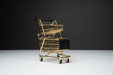 Beyaz masanın üstünde altın renkli küçük boş alışveriş arabası veya metal tramvay ve fotokopi alanı olan koyu arkaplan.