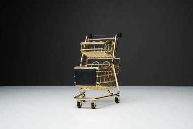 Beyaz masanın üstünde altın renkli küçük boş alışveriş arabası veya metal tramvay ve fotokopi alanı olan koyu arkaplan.