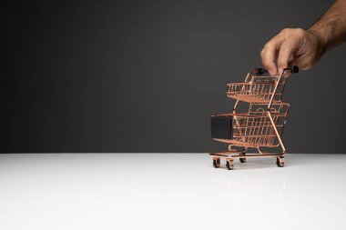 Küçük boş bir alışveriş arabasını itin veya bakır renkli bir tramvay beyaz masanın üstüne ve koyu arkaplan fotokopi alanı ile.