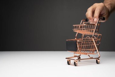 Küçük boş bir alışveriş arabasını itin veya bakır renkli bir tramvay beyaz masanın üstüne ve koyu arkaplan fotokopi alanı ile.