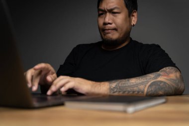 Asyalı adam dizüstü bilgisayarı kullanıyor, yüzü tahta masaya odaklı ve dizüstü bilgisayarı var. Evde çalışma kavramı.