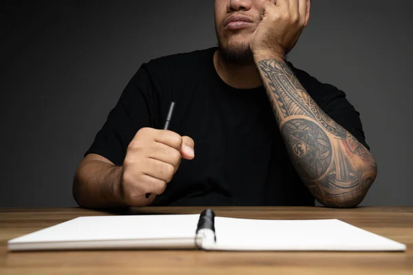 Asian man writing on a note book with thinking face on wooden table. Concept about work remotely.