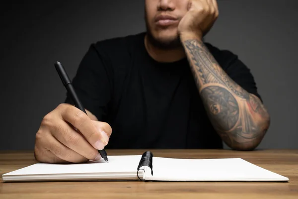 Asian man writing on a note book with boring face on wooden table. Concept about work remotely.