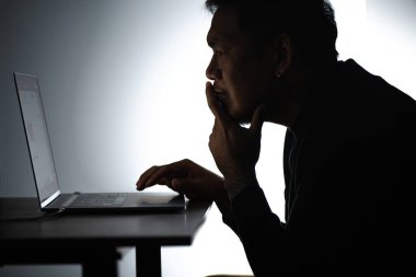 Laptop 'ta çalışan Asyalı siluet adam. Beared Man, Notebook 'ta evden çalışıyor. Serbest çalışan blogcu adam dizüstü bilgisayarla evde çalışıyor. Bakan ve odaklanan bir adam.