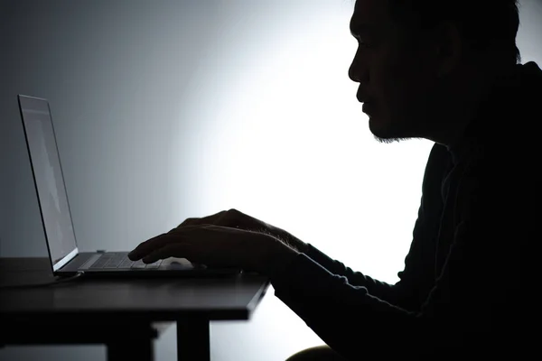 Silhouette asian man Working on Laptop. Beared man Works from home on Notebook. Freelancer man Blogger Working remotely at Home With Laptop. A Man looking and focusing face.