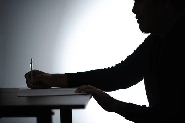 Silhouette asian man writing on table. Beared man writing on Notebook. Freelancer man Blogger writing at Home on desk.