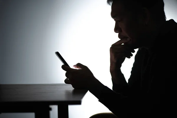 Siluet Asyalı adam akıllı telefon üzerinde çalışıyor. Beared Man cep telefonuyla evden çalışıyor. Ev 'de cep telefonuyla çalışan serbest çalışan blogcu adam. Bakan ve düşünen bir adam.