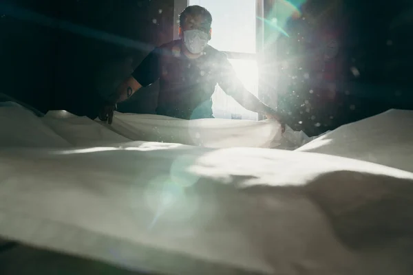 Asian man cleaning bed in morning. House keeping action. Bedroom gainst the sun light.