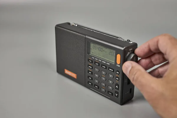 Adamın eli küçük bir radyo alıcısını ayarlıyor.
