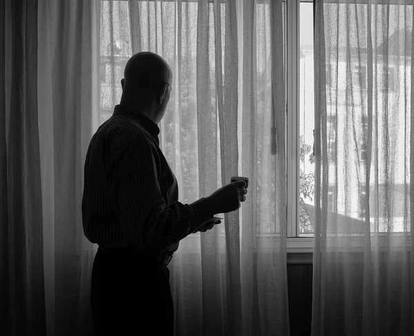 Man looks out the window of a building during confinement due to the COVID-19 coronavirus