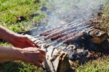 Erkek elleri doğada kömürün üzerinde kebap ile şişleri düzeltir. Yakın plan..