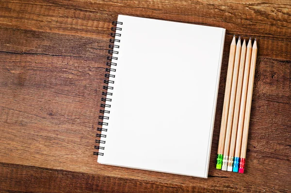 Cuaderno abierto en blanco con muchos lápices de madera . — Foto de Stock