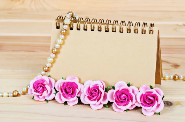 Notebook vazio marrom em branco com rosas cor-de-rosa sobre fundo de madeira . — Fotografia de Stock