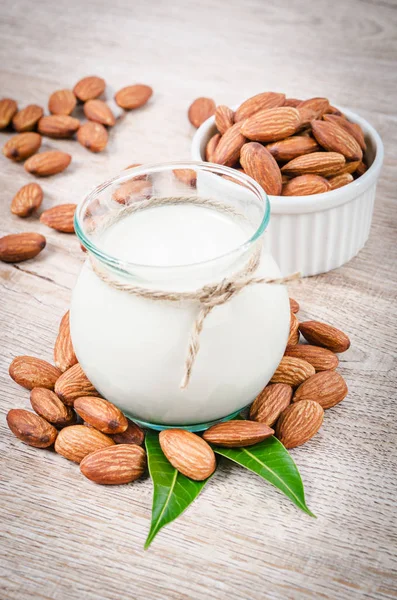 Almond milk and dry almond nuts with green leaf. — Stock Photo, Image