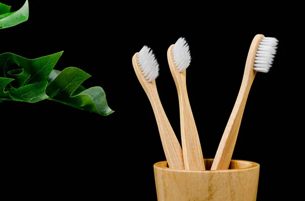 Bamboo toothbrushes with green leaves on black background. — Stock Photo, Image