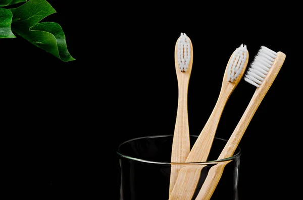 Bamboo toothbrushes with green leaves on black background. — Stock Photo, Image
