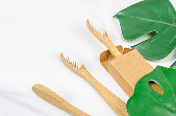 Bamboo toothbrushes with green leaves on marble background. — Stock Photo, Image