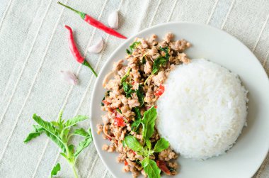 Rice topped with stir-fried pork and basil in dish.