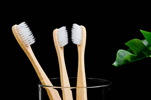 Escovas de dentes de bambu com folhas verdes no fundo preto . — Fotografia de Stock