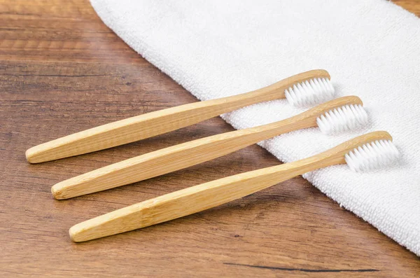 Bamboo toothbrushes with towel on wooden background. — Stock Photo, Image